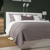 Greyscale PELARTUJA Tagesdecke auf dem Bett mit Kopfteil, Kissen, Hausschuhe auf Teppich, dunkelgrüne Wände, minimalistisches Dekor.