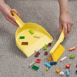 Kinder, die mit gelbem Pinsel bunte Spielzeugblöcke in eine gelbe Kehrschaufel fegen.