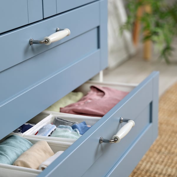 Blaue Kommodenschublade offen, in der ordentlich gefaltete Kleidung in Organizern zu sehen ist. Weiße Griffe sichtbar.