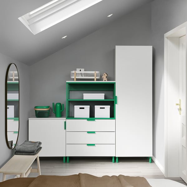 Modernes Schlafzimmer mit weißer und grüner PLATSA-Kommode, hohem weißem Schrank, Spiegel und Holzbank unter abgewinkelter Decke.