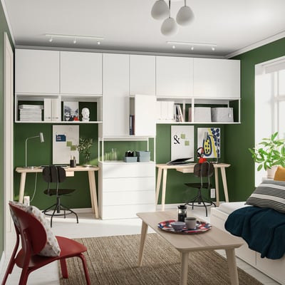 Modernes Home Office mit grünen Wänden, weißen PLATSA-Aufbewahrungseinheiten, Holzschreibtischen, schwarzen Bürostühlen, buntem Teppich und rotem Akzentstuhl.