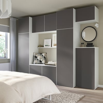 Modernes Schlafzimmer mit grauem PLATSA-Stauraum, weißem Bett, Spiegel, geometrischem Kissen.