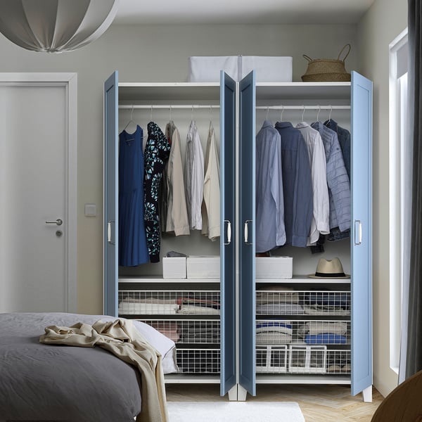Schlafzimmer mit blauem PLATSA-Kleiderschrank, hängender Kleidung, Regalen und Aufbewahrungskörben.