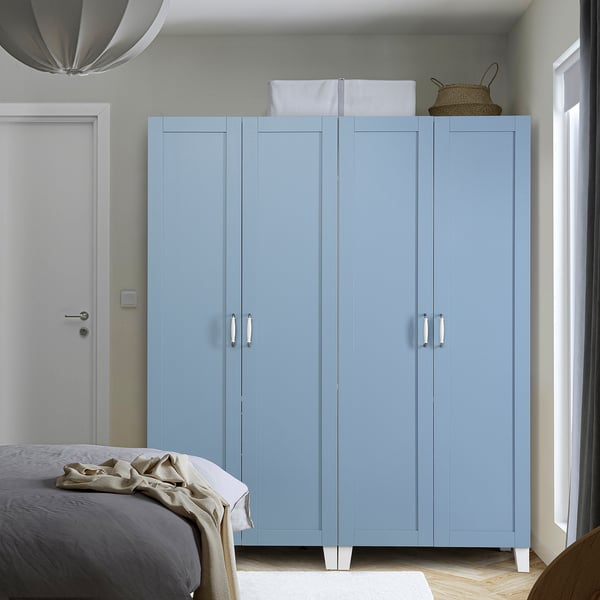 Großer blauer PLATSA-Kleiderschrank im Schlafzimmer, größer als das nahegelegene Bett, weiße Griffe, helles Dekor.