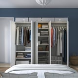 Offener Kleiderschrank mit Kleidung, gefalteter Kleidung und Accessoires, die darin organisiert sind. Regale und Kleiderbügel sind sichtbar und zeigen eine einfache Einrichtung.