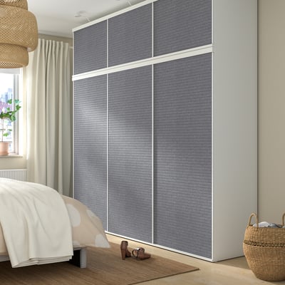 Modernes Schlafzimmer mit großem grauen PLATSA-Kleiderschrank, Schiebetüren, weißem Bett und Weidenkorb.