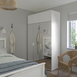 Modernes Schlafzimmer, hoher weißer PLATSA-Kleiderschrank und Bett mit heller Bettwäsche. Korbstuhl- und Spiegeltüren werten den Raum auf.