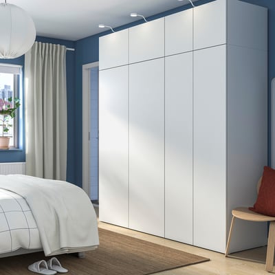 Minimalistisches Schlafzimmer mit großem weißem PLATSA-Kleiderschrank und kontrastierenden blauen Wänden. Inklusive Beet, Teppich, Hocker und Topfpflanze.