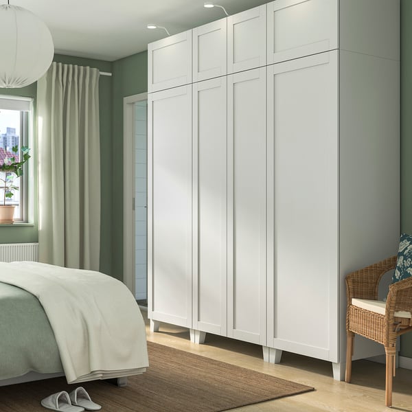 Modernes Schlafzimmer mit großem weißem PLATSA-Kleiderschrank, Korbstuhl, Bett und Pflanze. Der Kleiderschrank überragt andere Gegenstände.