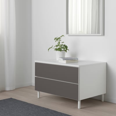 Moderner PLATSA-Stauraum mit 2 grauen Schubladen, weißer Platte, Pflanze, Büchern, vor weißer Wand.