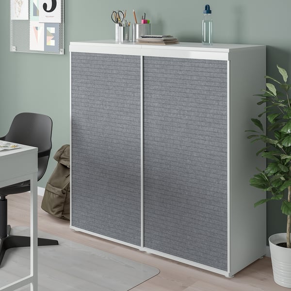 Weißer PLATSA-Schrank mit grauen Türen in der Home-Office-Ecke, höher als Schreibtisch, Wohngegenstände, Pflanze daneben.