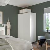 Weißer PLATSA-Kleiderschrank, groß und minimalistisch, vor dunkelgrüner Wand in der Nähe von Bett, Stuhl und Fenster.