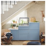 Modernes Zimmer mit blauem PLATSA-Stauraum unter der Treppe, mit Topfpflanzen und einem Korbstuhl.