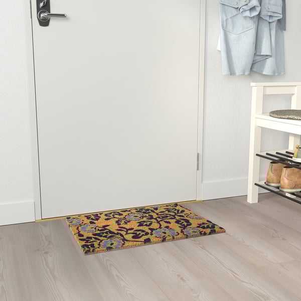 Blaue florale Türmatte in der Nähe der weißen Tür und des Schuhregals fängt Schmutz ein.