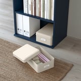Blaues Regal mit weißen Boxen zur Aufbewahrung von Akten und Büchern. Eine Schachtel öffnete sich auf dem Boden und gab den Blick auf farbige Ordner frei.