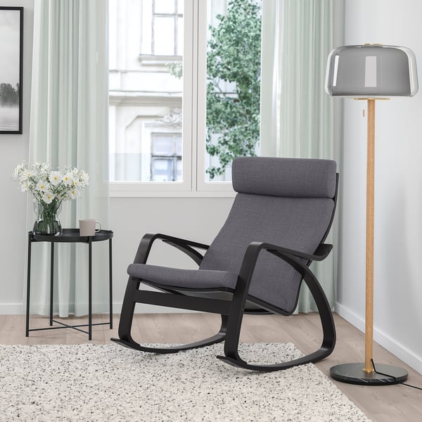 Modernes Wohnzimmer mit schwarzem POÄNG Schaukelstuhl, Holzlampe, grauen Vorhängen und Blumen.