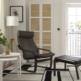 Modernes Wohnzimmer mit schwarzem POÄNG-Relaxsessel, Fußhocker, Beistelltisch, geflochtenem Schrank, Kunst, geometrischem Teppich.