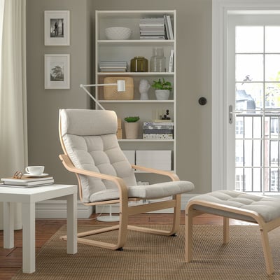 Wohnzimmer mit POÄNG Sessel, Fußhocker, Bücherregal, Fenster.