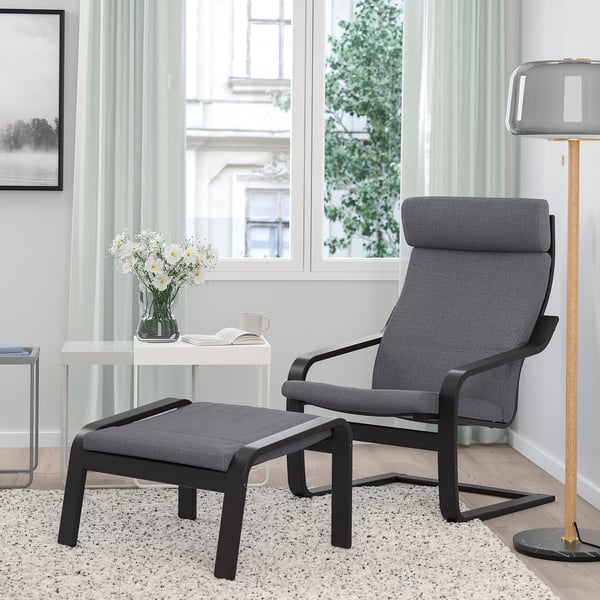 Gemütliches Wohnzimmer mit grauem POÄNG Sessel, Fußhocker, Beistelltisch, hoher Lampe, großen Fenstern, warmem Teppich.