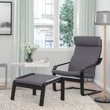 Gemütliches Wohnzimmer mit grauem POÄNG Sessel, Fußhocker, Beistelltisch, hoher Lampe, großen Fenstern, warmem Teppich.