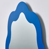 Blauer Spiegel mit gewellten Kanten an der Wand, lebendig, gut verarbeitet, Sicherheitsfolie sichtbar.
