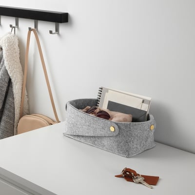 Grauer Aufbewahrungskorb aus Filz auf dem Schreibtisch mit Sonnenbrille, Schlüsseln und Notizbüchern. Platzsparend flach zusammenklappbar.