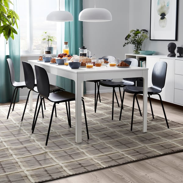 Modernes Esszimmer mit braun/grauem Schottenholz-Wollteppich, weißem Tisch und schwarzen Stühlen, blaugrünen Vorhängen und Dekorationsartikeln.