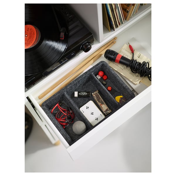 Schwarze und graue Filzorganizer in einer weißen Schublade mit verschiedenen kleinen Gegenständen wie Kabeln, USB-Laufwerken und einem Mikrofon.