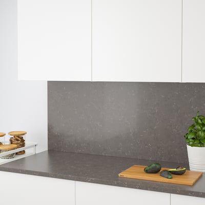 Moderne Küche mit grauer Quarz-Arbeitsplatte und Spritzschutz. Avocados und Schneidebrett auf der Theke, Gläser links, Pflanze rechts.