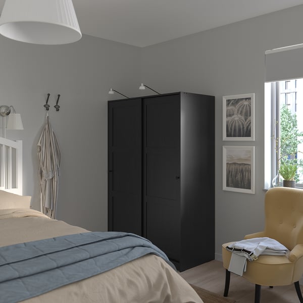 Schlafzimmer mit grauen Wänden, einem schwarzen Kleiderschrank von RAKKESTAD, einem gelben Stuhl und einem weißen Bett mit blauer Decke.