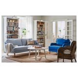 Helles Wohnzimmer mit blauem Sofa, Korbstuhl und Bücherregalen mit Büchern und Lampen.