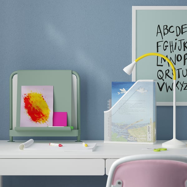 Schreibtisch mit RELATERA-Leuchte, Tafel, Organizer. Gelbes Bogenlicht, bunte Tafel, Bücher.