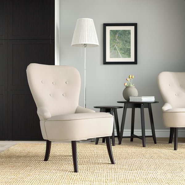 Modernes Wohnzimmer mit 2 beigen Stühlen, schwarzen Akzenten, grauen Wänden, Naturteppich, Lampe und Beistelltisch. Gemütlich und zeitgemäß.