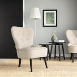 Modernes Wohnzimmer mit 2 beigen Stühlen, schwarzen Akzenten, grauen Wänden, Naturteppich, Lampe und Beistelltisch. Gemütlich und zeitgemäß.