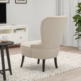 Beigefarbener Sessel mit Holzbeinen auf einem gesprenkelten Teppich in einem Wohnzimmer, der eine Lendenwirbelstütze mit einem glatten, einladenden Bezug bietet.