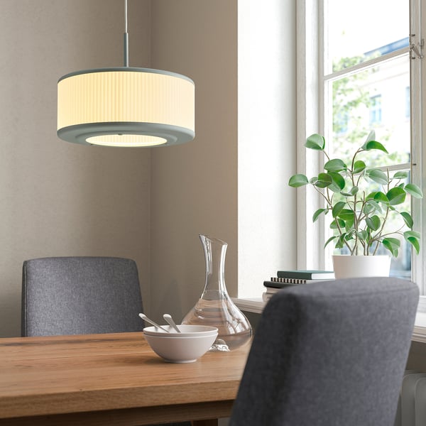 Cremefarbene Lampe über hölzernem Esstisch mit grauen Stühlen und Pflanze.
