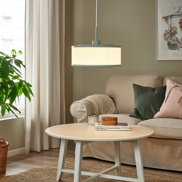Modernes Wohnzimmer mit grüner REMTÅNG-Pendelleuchte, weißem Couchtisch, grüner Couch und Pflanze am Fenster.