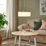 Modernes Wohnzimmer mit grüner REMTÅNG-Pendelleuchte, weißem Couchtisch, grüner Couch und Pflanze am Fenster.