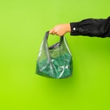 Grüne Netztasche mit Hand, perfekt für Fitnessstudio oder Schwimmen, befestigt an einer hellgrünen Wand.