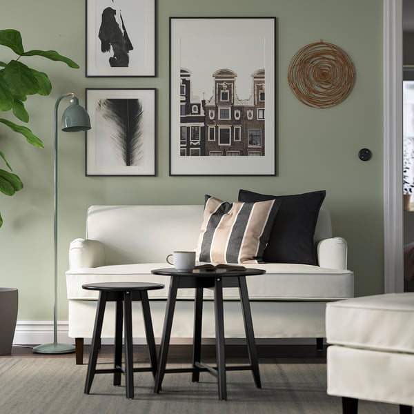 Minimalistisches Wohnzimmer: weißes Sofa, schwarze Beistelltische, grüne Wand mit Kunst, gemütliche Einrichtung.