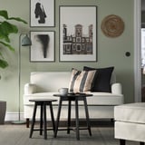 Minimalistisches Wohnzimmer: weißes Sofa, schwarze Beistelltische, grüne Wand mit Kunst, gemütliche Einrichtung.