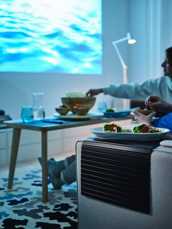 Menschen, die auf einem Sofa mit einem blauen Tablett essen. Das Sofa verfügt über ein Bambustablett für Snacks.