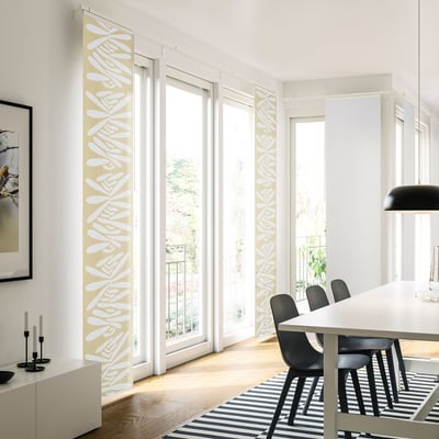 Modernes Esszimmer mit gelben Vorhängen mit Blattmuster, die das Licht streuen und eine lebendige Note verleihen. Schwarze Stühle, gestreifter Teppich und Pendelleuchte. ”