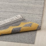 Flachgewebter Wollteppich mit geometrischem Muster und gelber Bordüre. Anti-Rutsch-Pad darunter für Sicherheit.