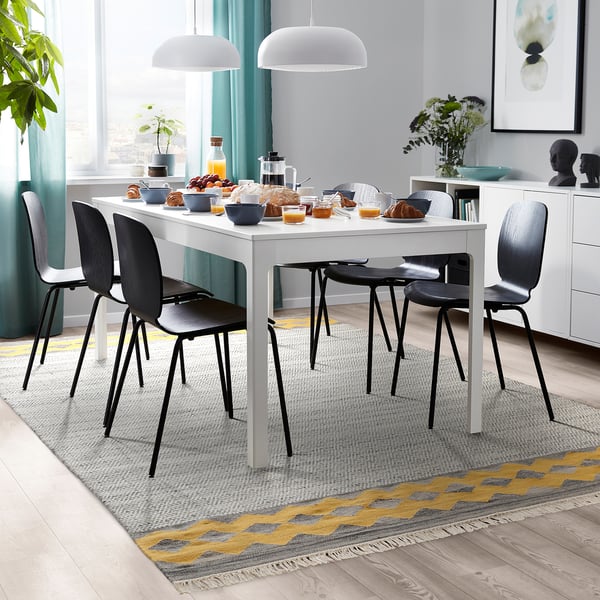 Moderner Essbereich mit weißem Tisch, schwarzen Stühlen, Essen, Trinken, Fenster, Pflanzen, Wollteppich.