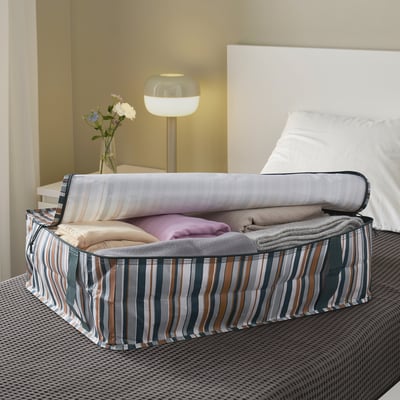 Eine Aufbewahrungsbox auf einem Bett mit gefalteten Decken und Kissen; Es ist waschbar und passt unter Betten.