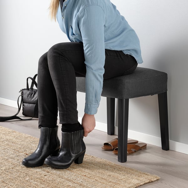Person in blauem Hemd und Stiefeln auf Hocker, Tasche in der Nähe.