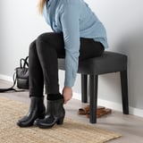 Person in blauem Hemd und Stiefeln auf Hocker, Tasche in der Nähe.