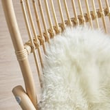 Das Bild zeigt einen handgeflochtenen Rattansessel mit einem flauschigen weißen Kissen, das das natürliche, robuste Design unterstreicht.