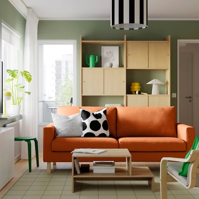 Gemütliches Wohnzimmer mit orangefarbenem Sofa, gepunkteten Kissen, Holzbücherregal, Pflanze, Couchtisch und gestreiftem Licht.